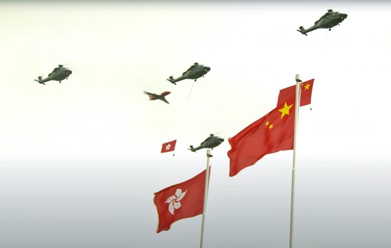 懸掛着國旗及區旗的直升機編隊飛過升旗禮會場上空。（中通社）