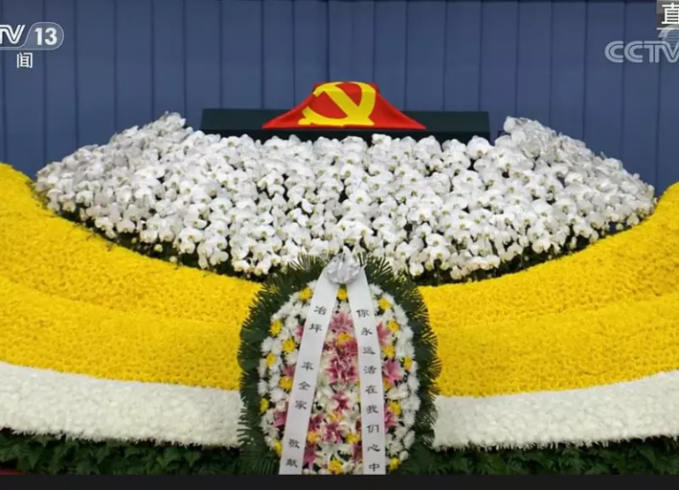 江澤民的骨灰用中共黨旗覆蓋，正前方花圈上輓聯寫着「你永遠活在我們心中」，落款人是江的遺孀王冶坪率全家。（央視新聞截圖）